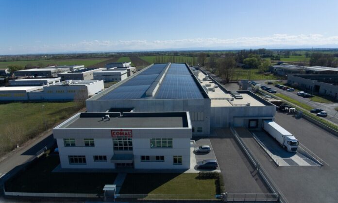 Aerial view of a large industrial facility with solar panels on the roof and delivery trucks at a loading dock.