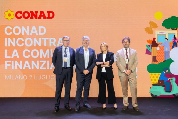 unnamed (7) Four professionals stand on a stage in front of a large orange CONAD backdrop with Italian text and logo, posing for a photo.