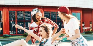 Il supermercato come destinazione: una sfida di identità per le insegne Three young friends laughing and pushing a shopping cart, with one girl sitting inside the cart and arms raised in excitement.