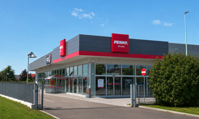 GHISALBA (1) Penny Ghislba supermarket exterior with red signage and glass entrance under a clear blue sky.