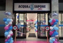 Cesar porta Acqua & Sapone a quota 150 punti vendita in Lombardia Storefront of Acqua e Sapone during a grand opening with pink carpet, blue and pink balloon columns, and a ribbon in front of glass doors.