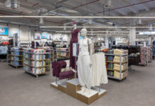 Primark apre a Parma Promenade il secondo negozio in Emilia-Romagna Store interior with mannequins wearing maroon and white outfits in the center, surrounded by shelves of folded clothes and a 'Womens' sign in the background.