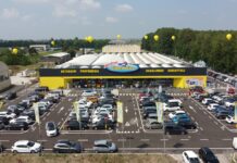 Aerial view of a large Megastore RisparmioCasa with a yellow-and-black facade and a crowded parking lot with many cars and yellow balloons above the building.