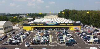 Aerial view of a large Megastore RisparmioCasa with a yellow-and-black facade and a crowded parking lot with many cars and yellow balloons above the building.