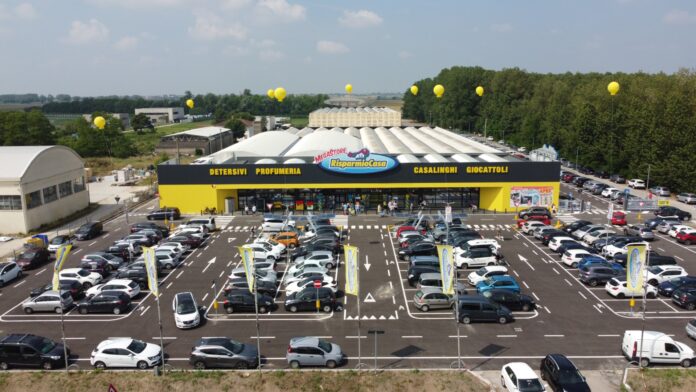 Aerial view of a large Megastore RisparmioCasa with a yellow-and-black facade and a crowded parking lot with many cars and yellow balloons above the building.