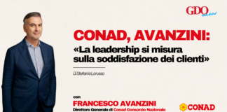 Conad, Avanzini: «La leadership si misura sulla soddisfazione dei clienti» Man in a navy suit on a beige background left of a bold Italian headline about leadership and customer satisfaction, with Conad and GDO News logos on the right.