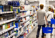 Action rafforza la presenza in Umbria con il nuovo store di Terni Shoppers with blue baskets walk down an aisle stocked with cosmetics and personal care products in a bright store.