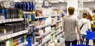 Action rafforza la presenza in Umbria con il nuovo store di Terni Shoppers with blue baskets walk down an aisle stocked with cosmetics and personal care products in a bright store.