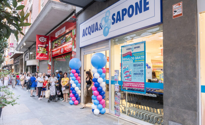 A&S Talavera-31 (1) People line up outside a Cosmopolitan-style shopfront with blue and white balloons decorating the entrance and a large ACQUA& SAPONE sign above the doorway, on a busy street.