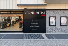 Storefront of Carni e Affini butcher and deli with a black sign listing Macelleria, Gastronomia, Frutta e Verdura, Enoteca.