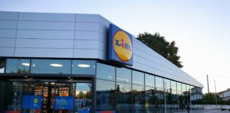 Front view of a Lidl supermarket with glass storefront and a prominent circular Lidl logo sign on the facade.