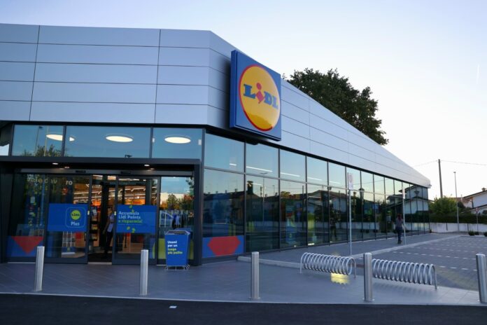 Front view of a Lidl supermarket with glass storefront and a prominent circular Lidl logo sign on the facade.