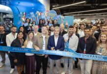 Primark apre a Pompei e raggiunge quota 500 store a livello globale Group of diverse people at a ribbon-cutting for Primark's 500th store, holding a blue 'PRIMARK' ribbon and small flags.