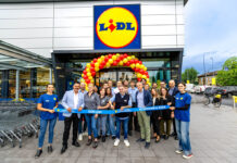Lidl aggiorna la rete in Romagna con il restyling del punto vendita di Lugo Group of Lidl staff and customers pose in front of the store under a red-yellow balloon arch, holding a blue ribbon reading '1306 Lugo' and '10 Settembre 2026'.
