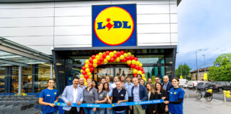 Lidl aggiorna la rete in Romagna con il restyling del punto vendita di Lugo Group of Lidl staff and customers pose in front of the store under a red-yellow balloon arch, holding a blue ribbon reading '1306 Lugo' and '10 Settembre 2026'.