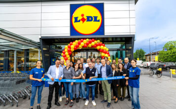 Lidl aggiorna la rete in Romagna con il restyling del punto vendita di Lugo Group of Lidl staff and customers pose in front of the store under a red-yellow balloon arch, holding a blue ribbon reading '1306 Lugo' and '10 Settembre 2026'.
