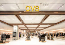 OVS apre a Dubai il più grande flagship store del Gruppo Bright clothing store interior with mannequins displaying outfits, circular display platforms, and racks of apparel under a white ceiling with wooden beams at the top of the aisle.
