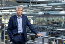 RATIONAL chiude il primo semestre 2026 con ricavi in crescita e conferma la guidance Executive in a navy suit standing on a mezzanine railing overlooking a manufacturing floor.