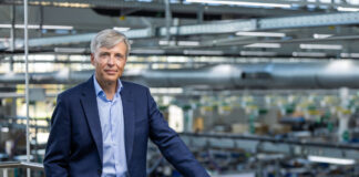 RATIONAL chiude il primo semestre 2026 con ricavi in crescita e conferma la guidance Executive in a navy suit standing on a mezzanine railing overlooking a manufacturing floor.