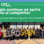 Eurospin continua ad aprire accanto ai competitor. Le nuove aperture seguono tutte lo stesso schema? Group of workers outside a building with a large green banner about Eurospin openings and gold EUROSPIN balloons in front.